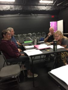 Actors and playwright sit around a table in the black box theater to read and review a new play script.