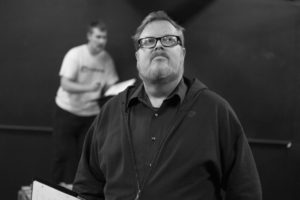 A black and white photo in which the actor playing Harrisson looks up from his script. 