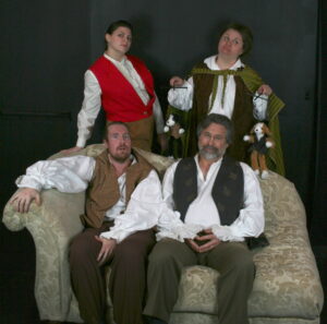 Confused Rosencrantz and Guildenstern sit on a couch while the Player and Alfred stand behind, knowingly.