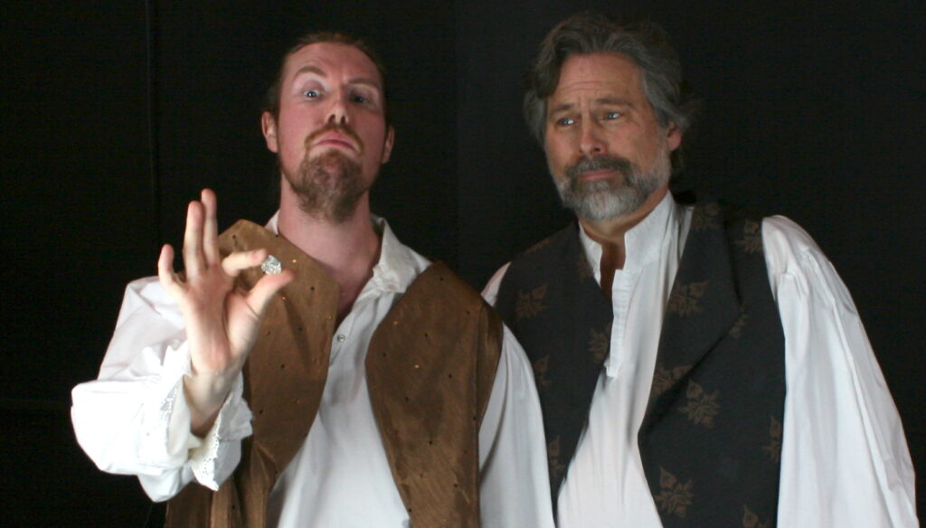 Rosencrantz holds up a coin to inspect with Guildenstern.