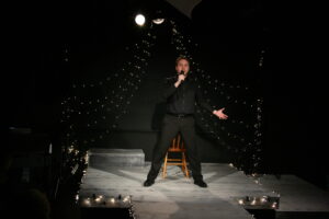 Renny holds a microphone to his mouth and stands in the spotlight for his Cabaret performance.
