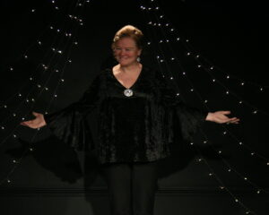 Amber stands on the stage at the Cabaret, dressed in all black, performing "I'm Still Here"