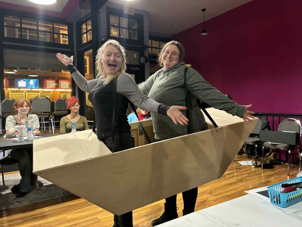 Two women wear a wooden boat that has been designed with shoulder straps so as to give the illusion they are riding the waves. 