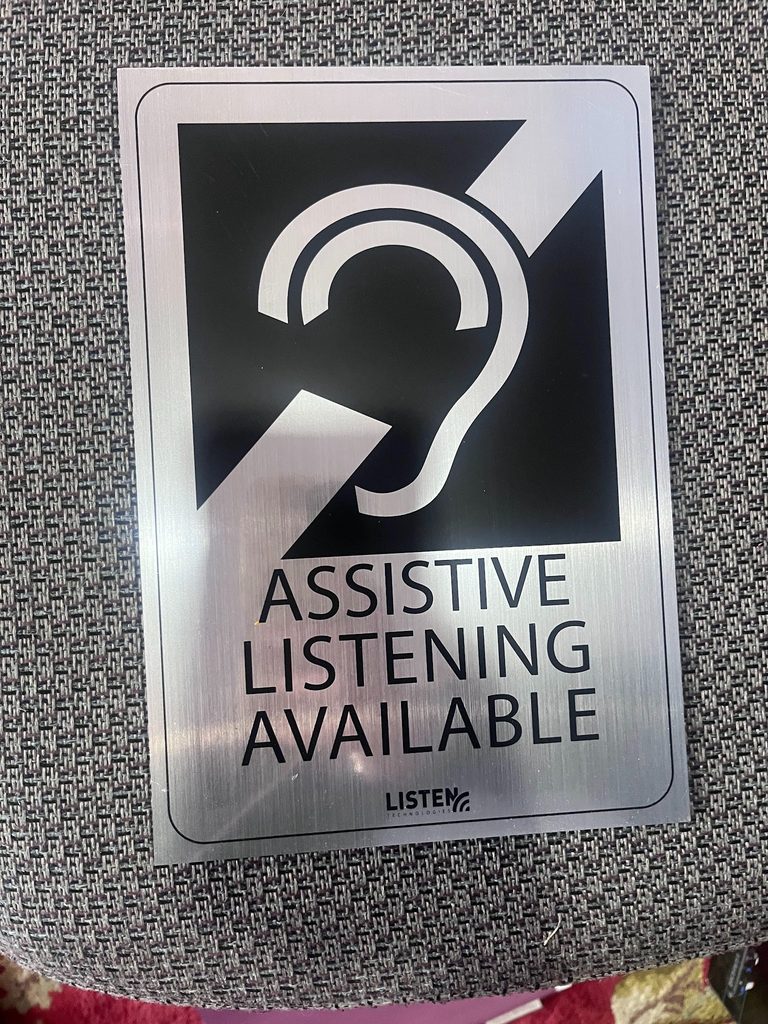 Silver sign with universal hearing access symbol which reads Assistive Listening Device Available